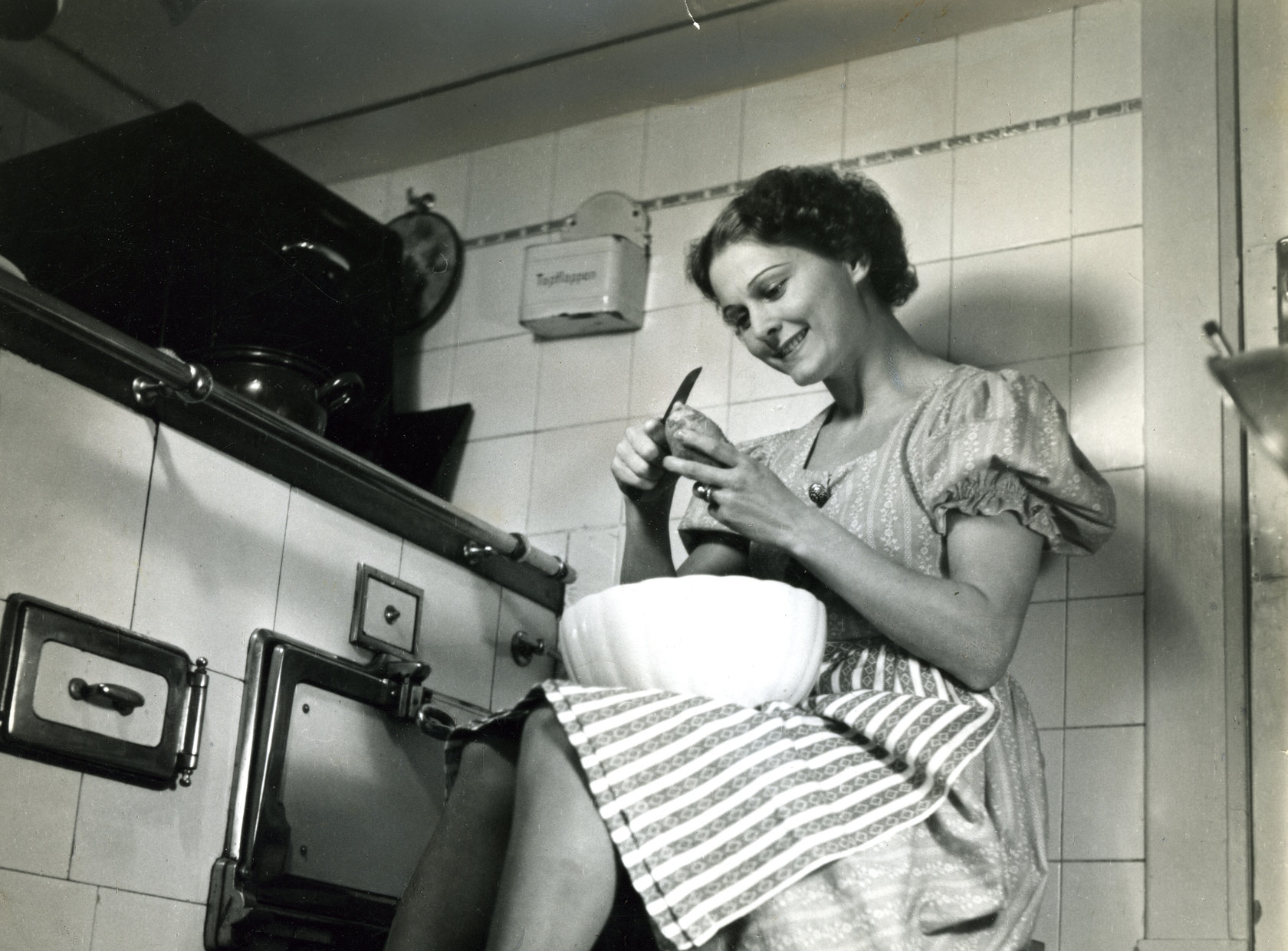 Schwarz-Weiß-Foto aus Photo Archiv Schweitzer: Frau schält Kartoffeln vor Küchenherd