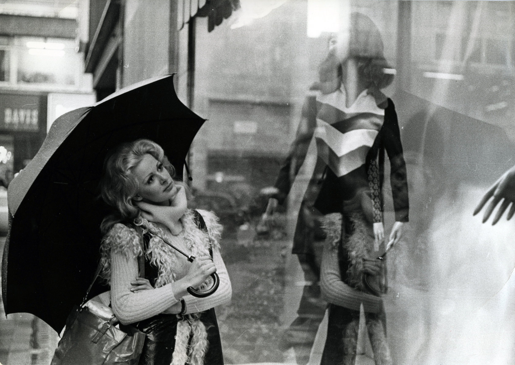Frau unter Regenschirm vor Auslage mit Schaufensterpuppe